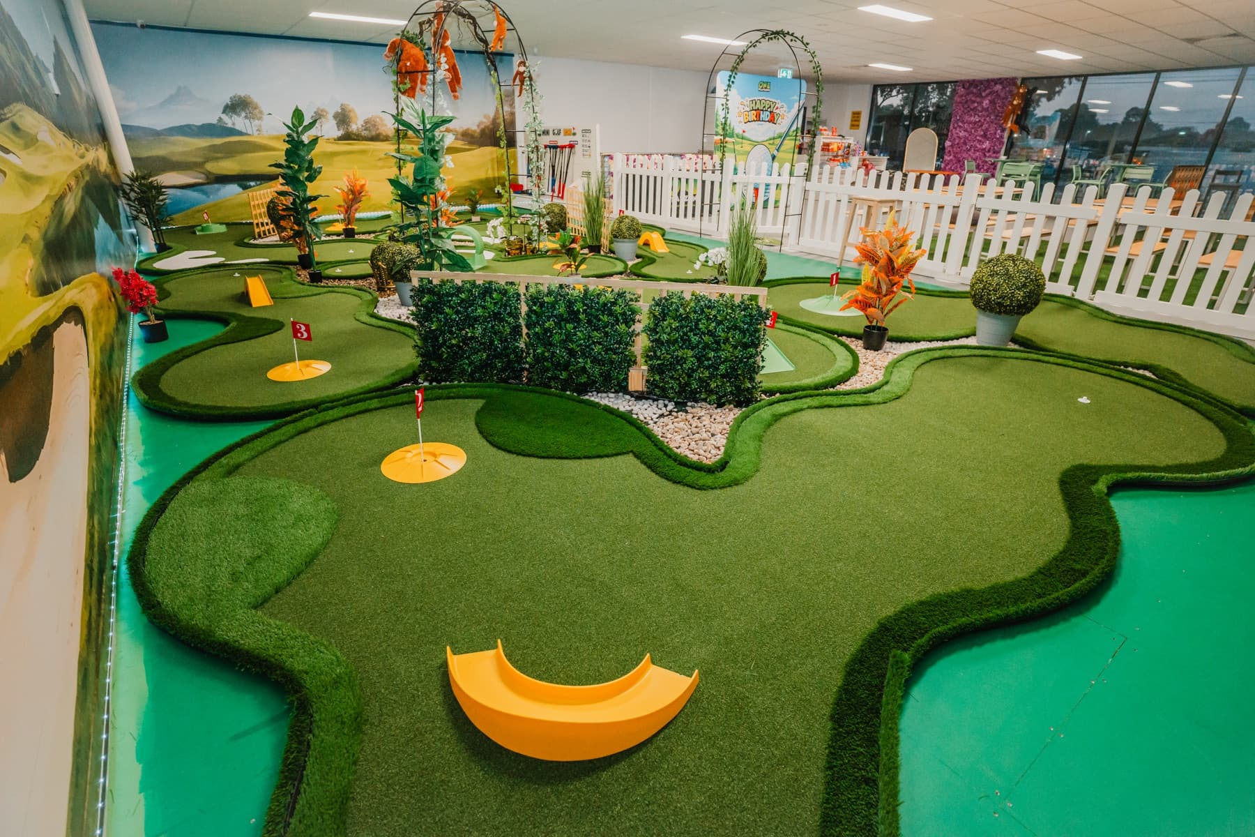 Photograph across the real nine-hole course with dark-green turf, red flags and white fence